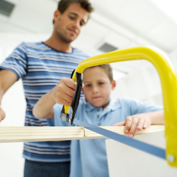 Boy Sawing Piece of Wood in Half with His Father --- Image by © Royalty-Free/Corbis