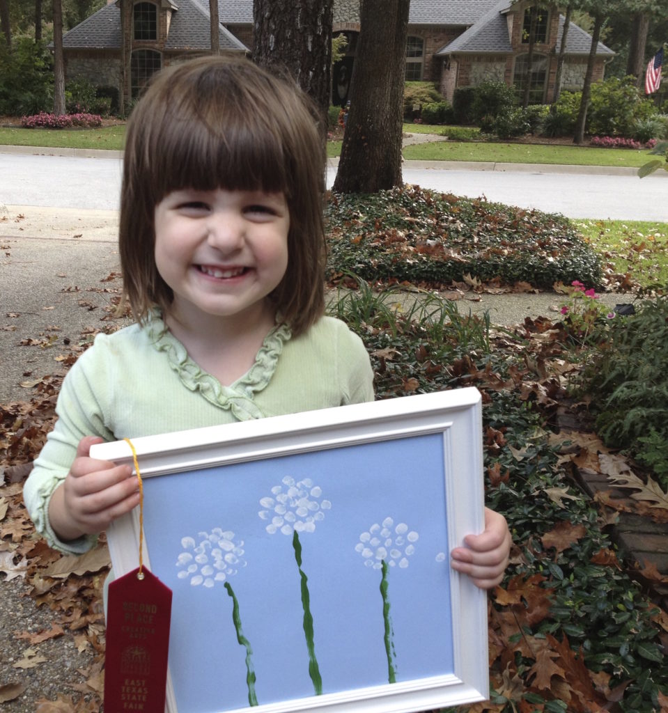 Abby shows off her prize-winning fingerpainting for the State Fair Creative Arts Contest .